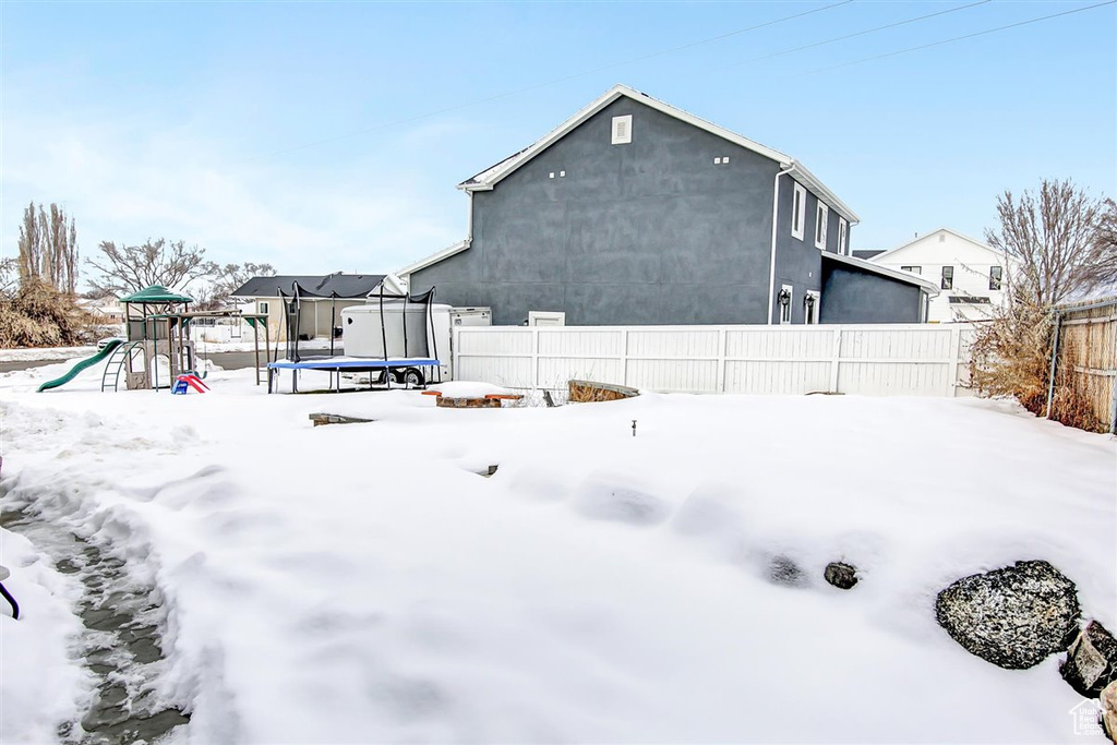 Snow covered back of property with a trampoline and a playground