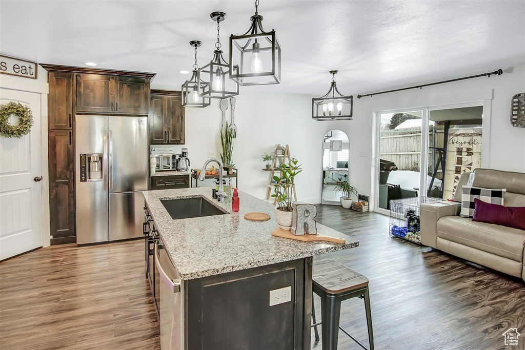 Kitchen with stainless steel fridge, light stone countertops, hanging light fixtures, dark hardwood / wood-style floors, and sink