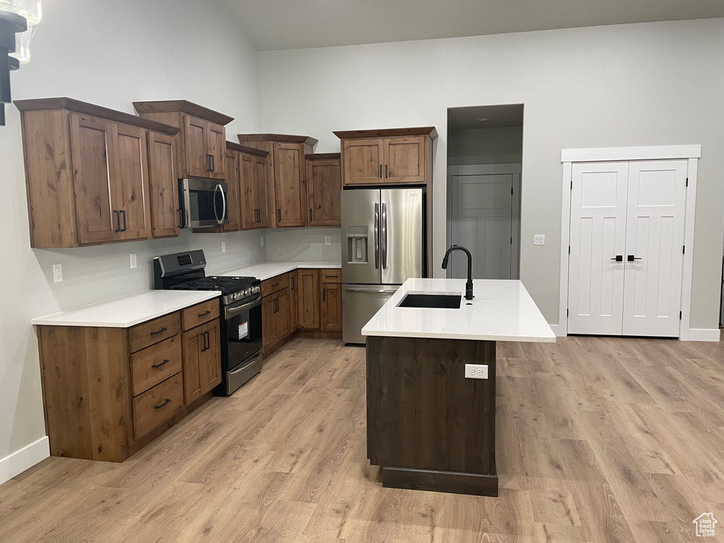 Kitchen with dark brown cabinetry, appliances with stainless steel finishes, light hardwood / wood-style flooring, an island with sink, and sink