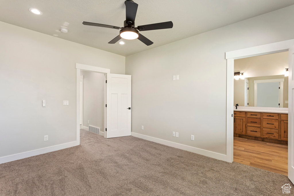 Unfurnished bedroom with light colored carpet, ensuite bathroom, and ceiling fan