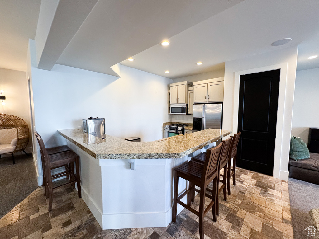 Kitchen featuring stainless steel appliances, dark colored carpet, and a kitchen bar