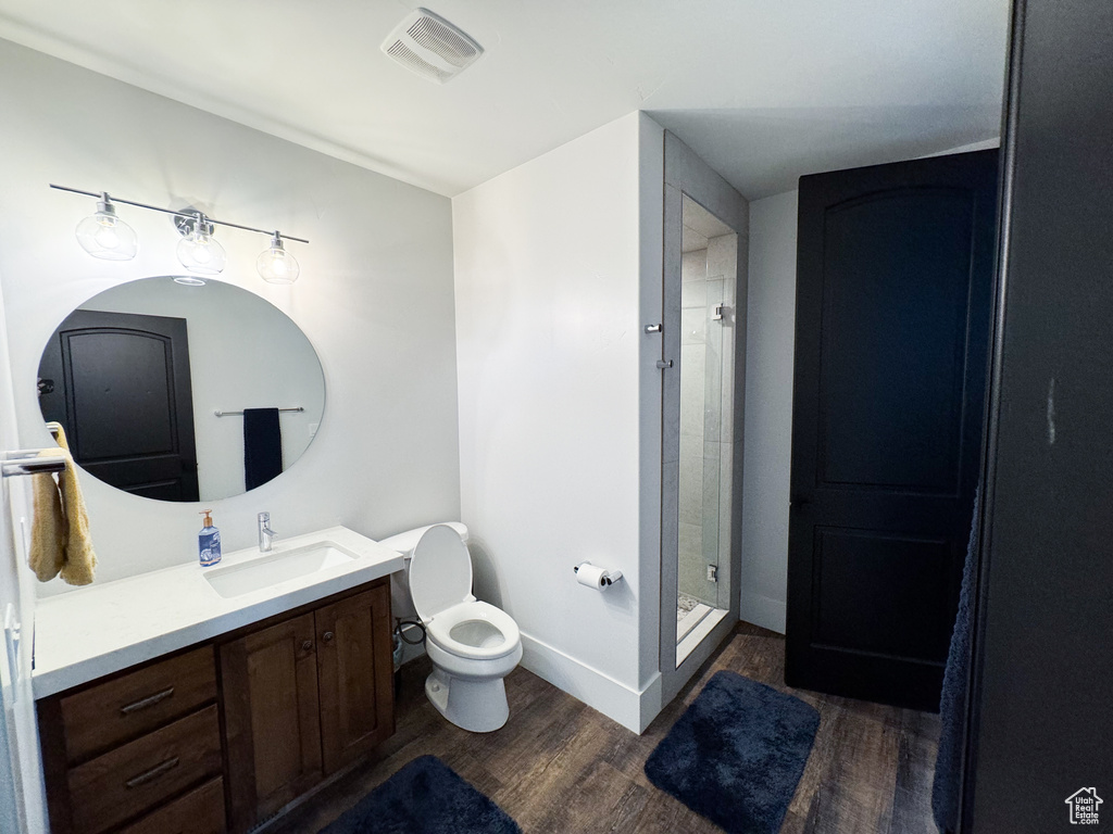 Bathroom featuring tiled shower, hardwood / wood-style floors, vanity, and toilet