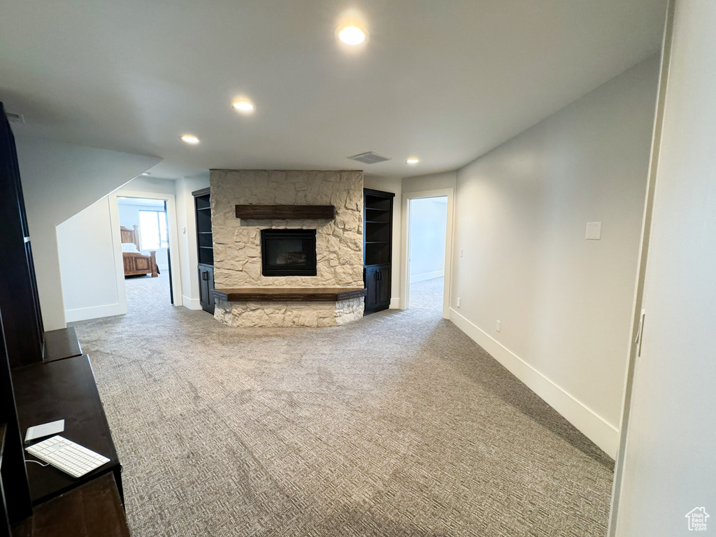 Unfurnished living room with a stone fireplace and light colored carpet