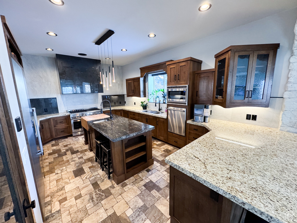 Kitchen featuring light stone countertops, appliances with stainless steel finishes, pendant lighting, and a center island with sink