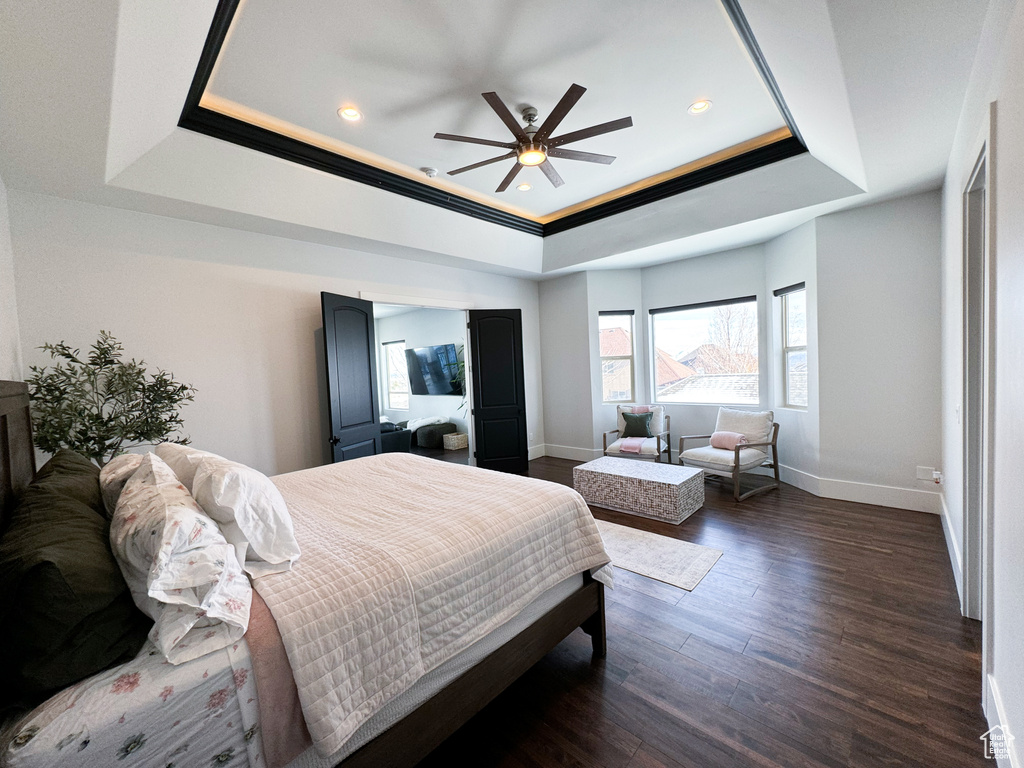 Bedroom with dark hardwood / wood-style flooring, ceiling fan, and a raised ceiling