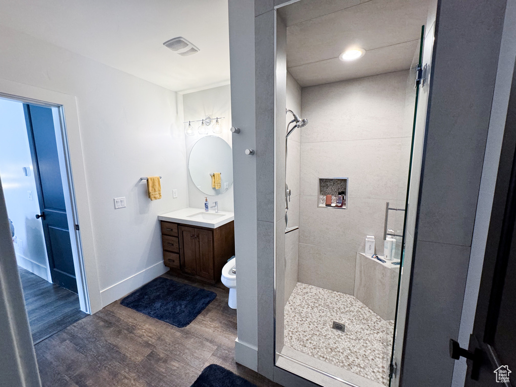 Bathroom featuring wood-type flooring, a tile shower, vanity, and toilet