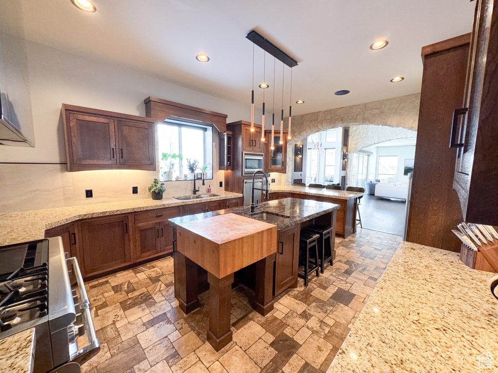 Kitchen featuring a breakfast bar area, a kitchen island with sink, decorative light fixtures, sink, and stainless steel microwave
