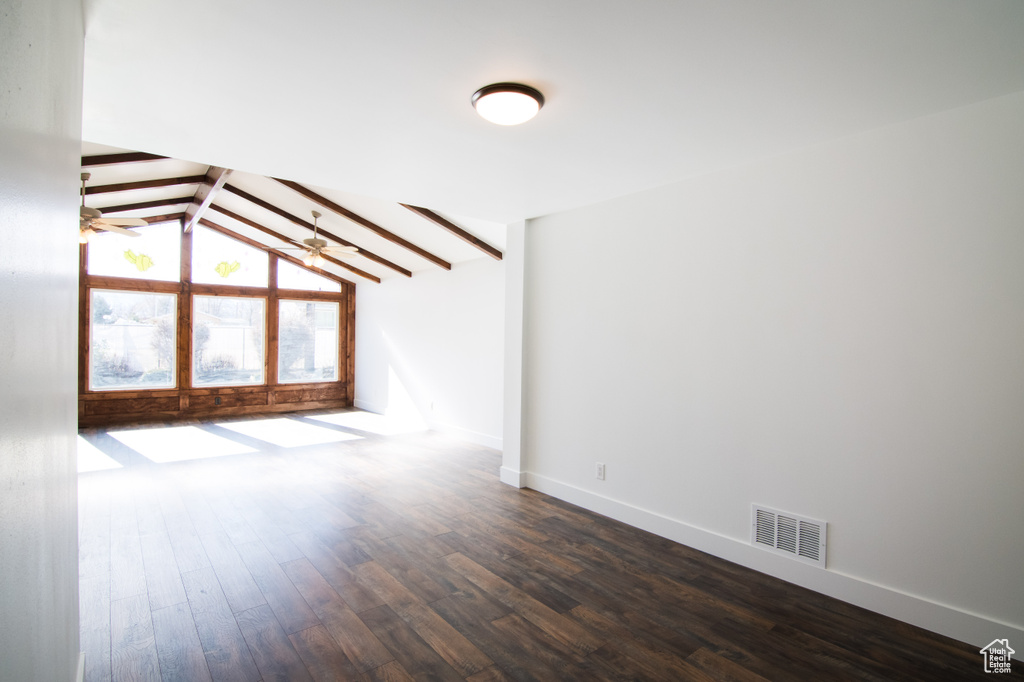 Empty room featuring lofted ceiling with beams, dark hardwood / wood-style flooring, and ceiling fan