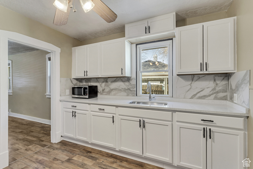 Kitchen featuring ceiling fan, tasteful backsplash, white cabinetry, sink, and hardwood / wood-style flooring