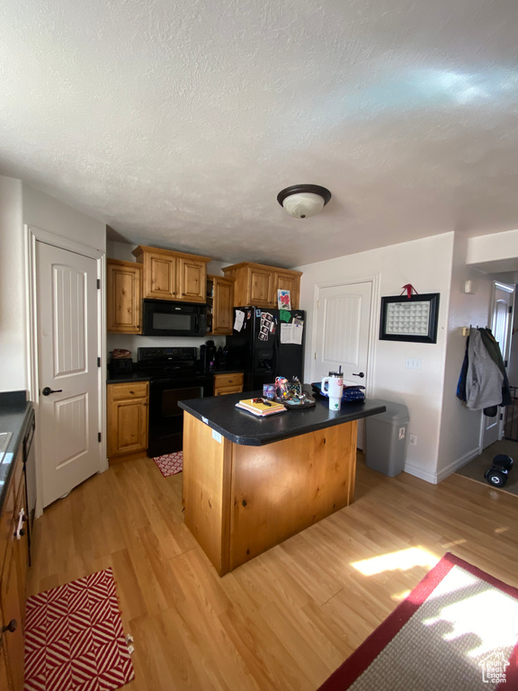 Kitchen with light hardwood / wood-style floors, a kitchen breakfast bar, a kitchen island, and black appliances