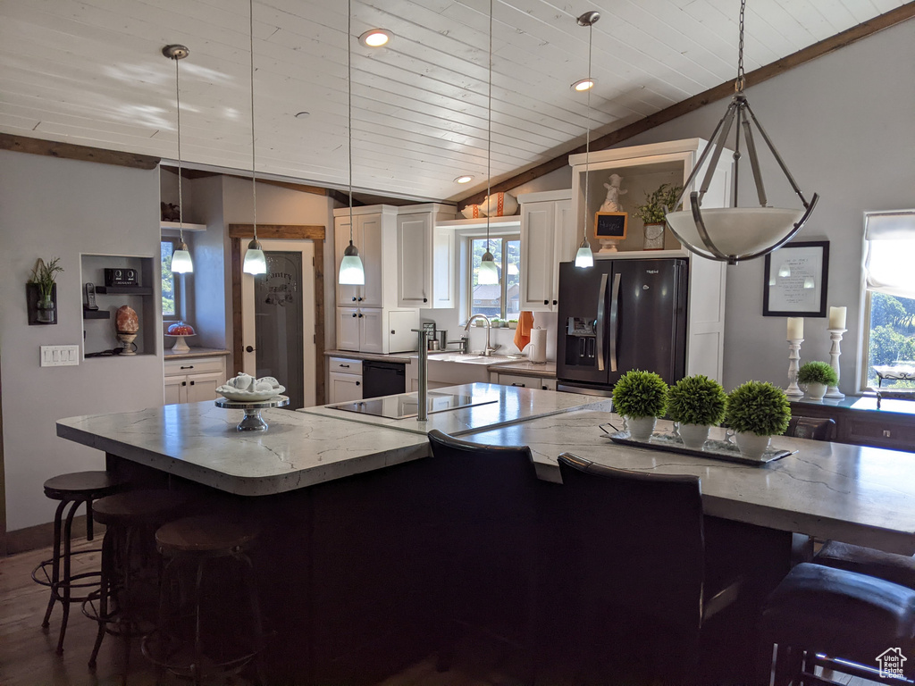 Kitchen with vaulted ceiling, a kitchen breakfast bar, white cabinets, hanging light fixtures, and black appliances