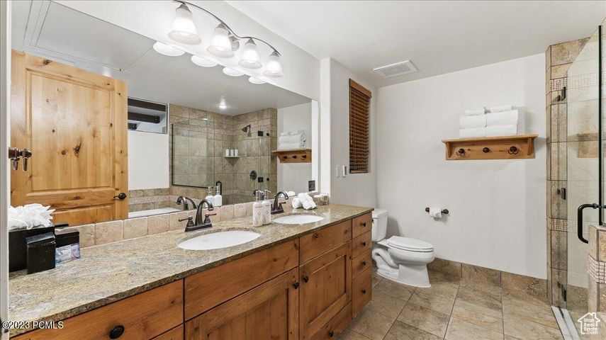 Bathroom with toilet, large vanity, tile floors, double sink, and walk in shower