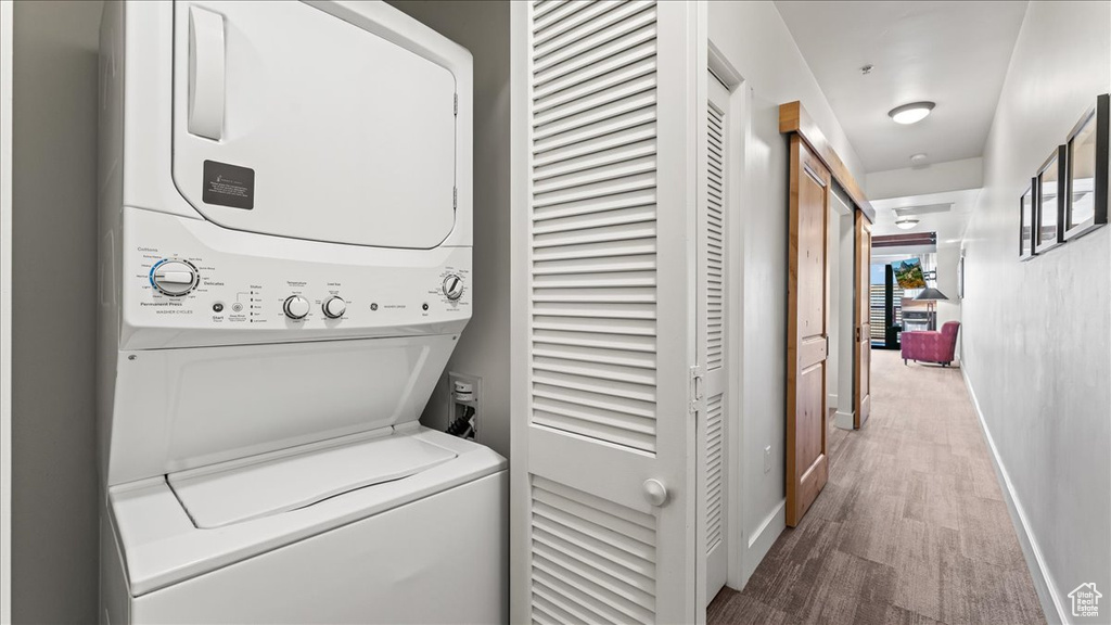 Clothes washing area with hardwood / wood-style floors and stacked washer / dryer