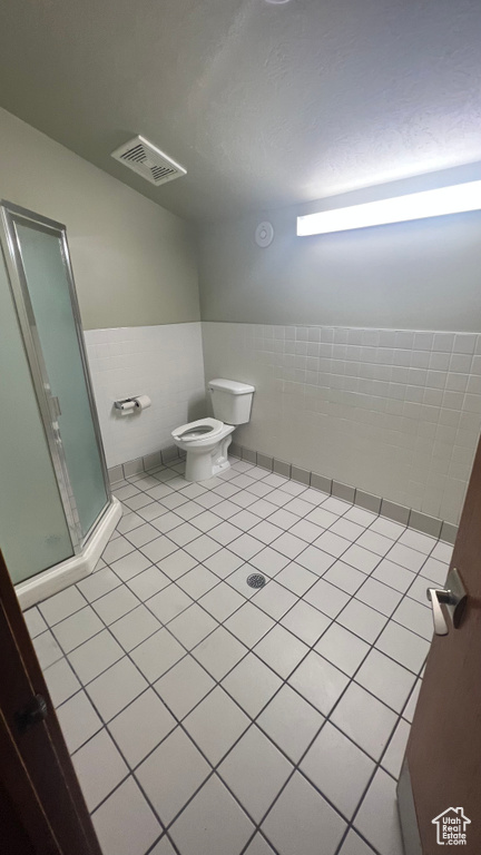 Bathroom with tile walls, toilet, tile flooring, and walk in shower