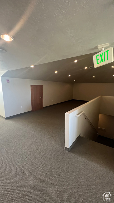 Interior space with dark colored carpet and lofted ceiling