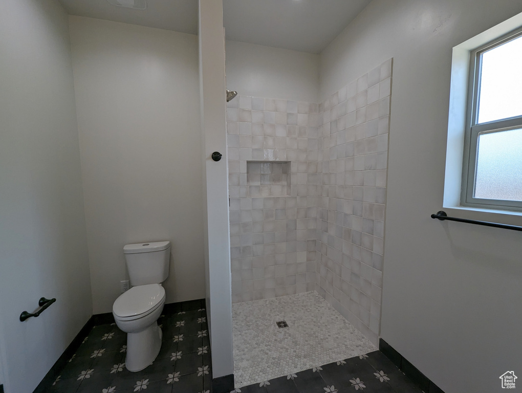 Bathroom featuring tiled shower, toilet, and tile flooring