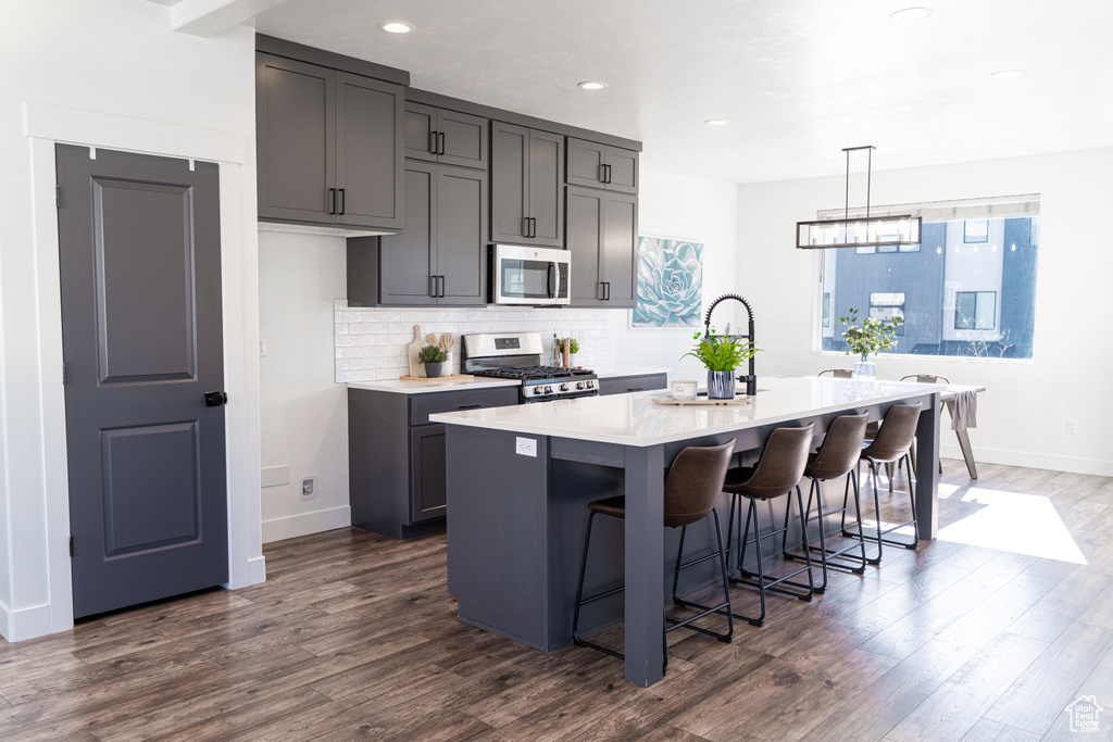 Kitchen with decorative light fixtures, dark hardwood / wood-style flooring, stainless steel appliances, a kitchen bar, and a center island with sink