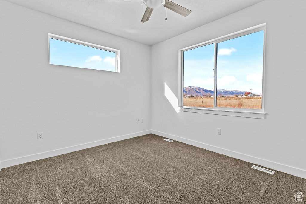 Empty room with a wealth of natural light, dark colored carpet, and ceiling fan
