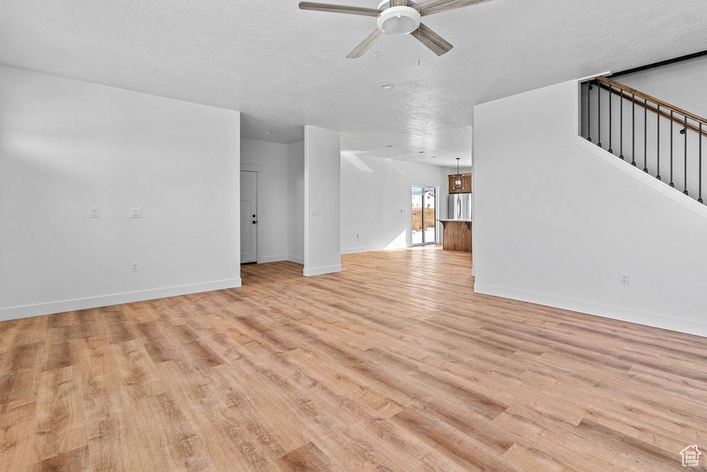 Unfurnished living room with light wood-type flooring, a textured ceiling, and ceiling fan