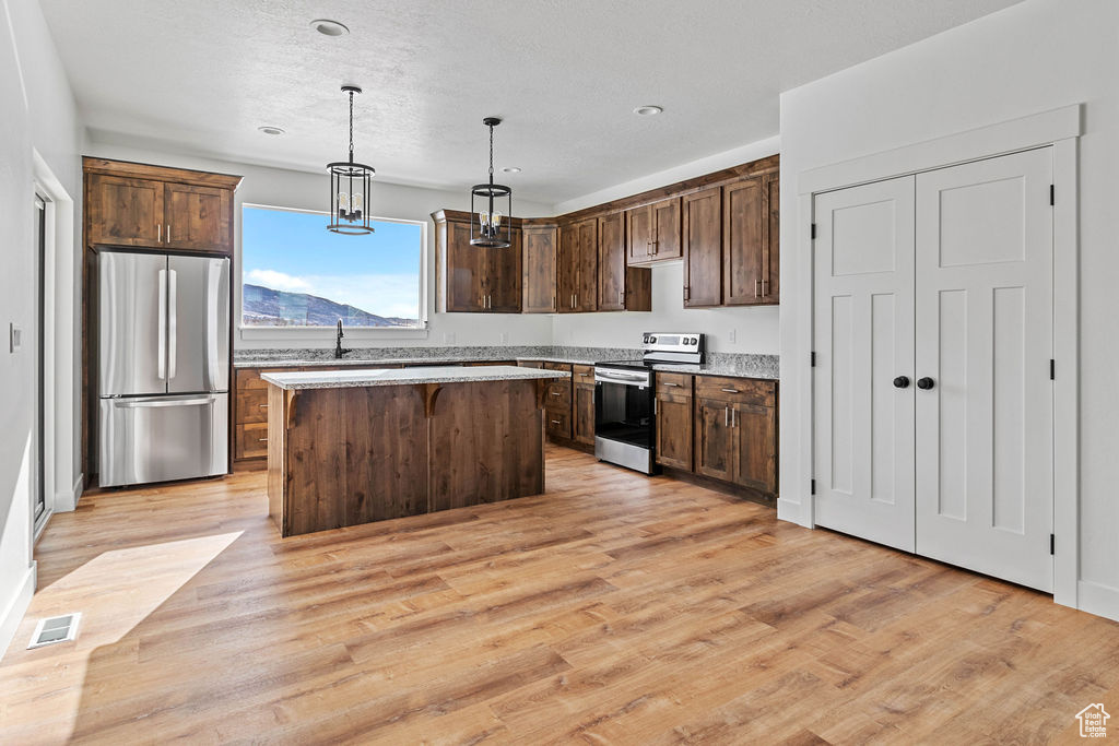 Kitchen featuring stainless steel refrigerator, range with electric cooktop, a kitchen island, hanging light fixtures, and light hardwood / wood-style flooring