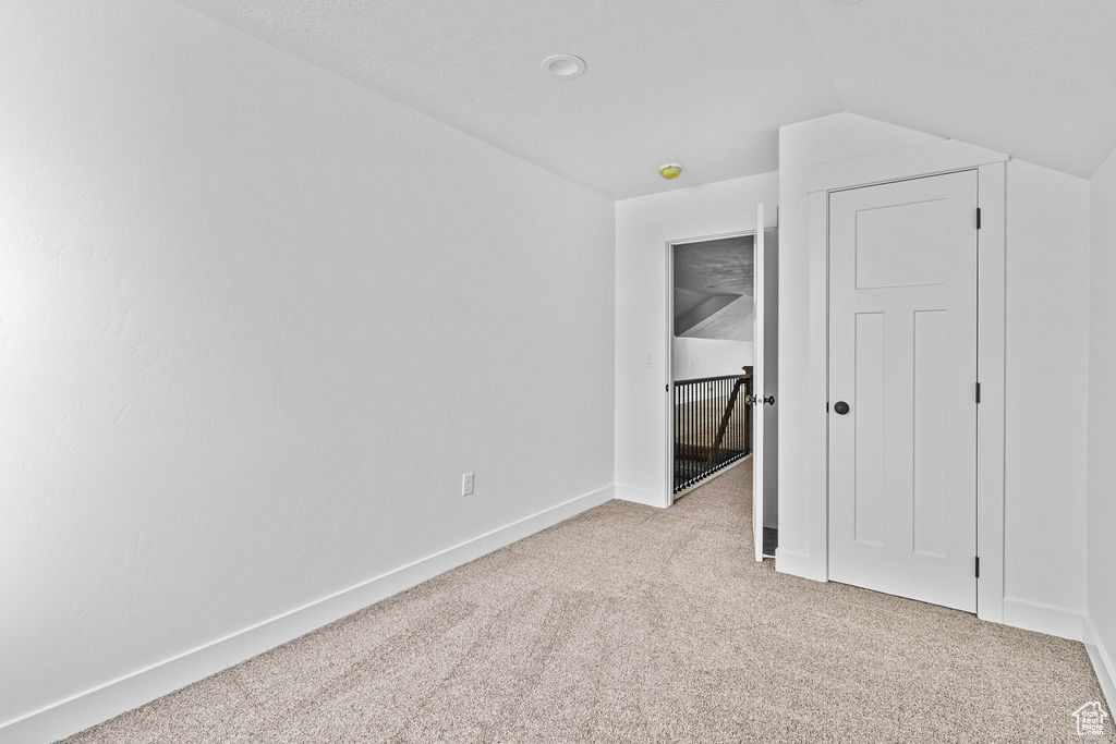 Unfurnished bedroom featuring lofted ceiling, a textured ceiling, and light colored carpet