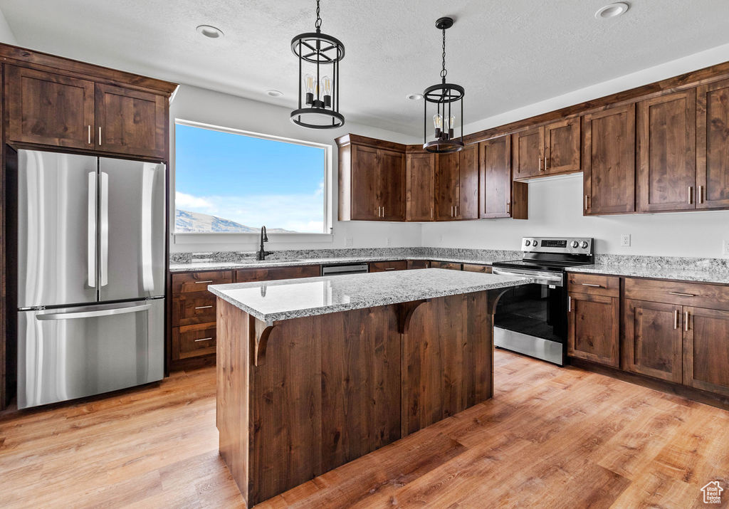 Kitchen with a breakfast bar, hanging light fixtures, appliances with stainless steel finishes, light stone counters, and light wood-type flooring