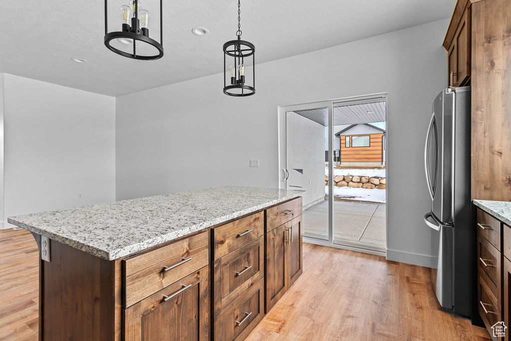 Kitchen featuring stainless steel fridge, light wood-type flooring, a kitchen island, and decorative light fixtures