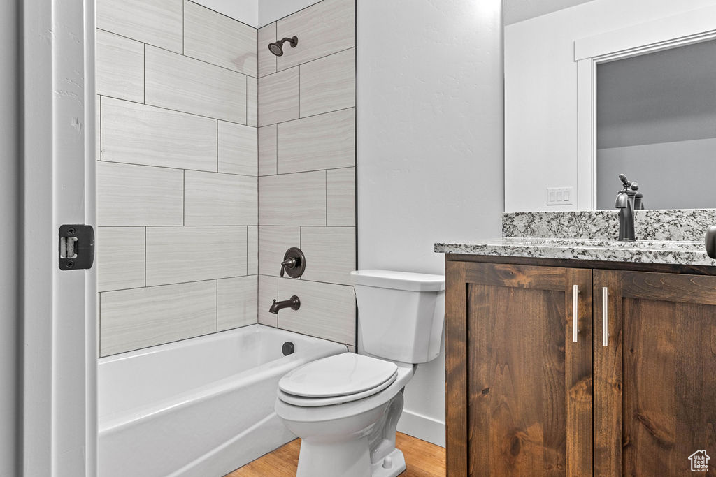 Full bathroom with vanity, tiled shower / bath combo, toilet, and hardwood / wood-style floors