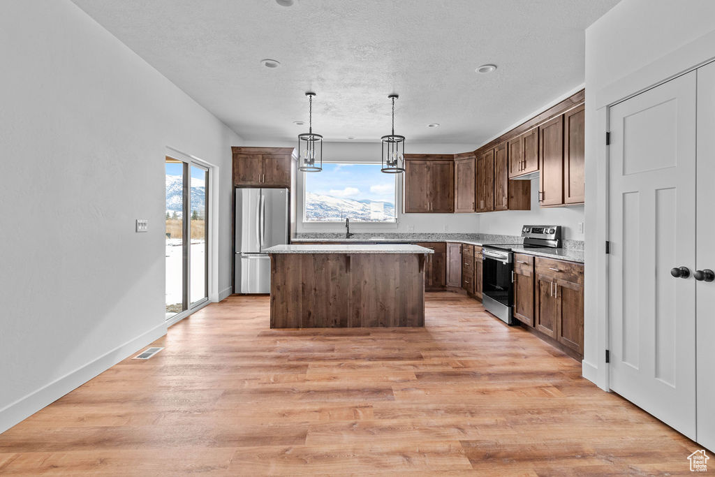 Kitchen with a center island, light hardwood / wood-style flooring, stainless steel appliances, and decorative light fixtures