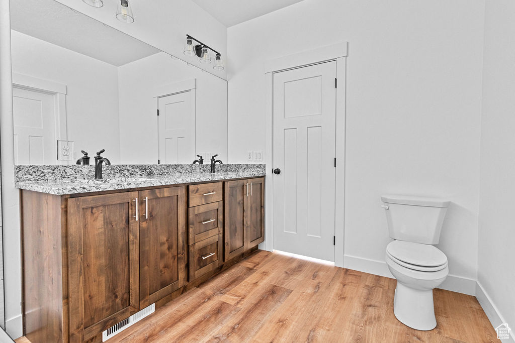 Bathroom featuring wood-type flooring, double vanity, and toilet
