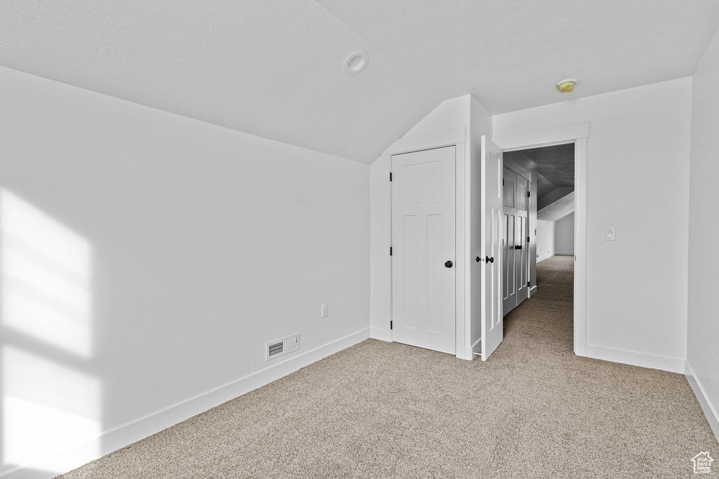 Unfurnished bedroom featuring light colored carpet and lofted ceiling