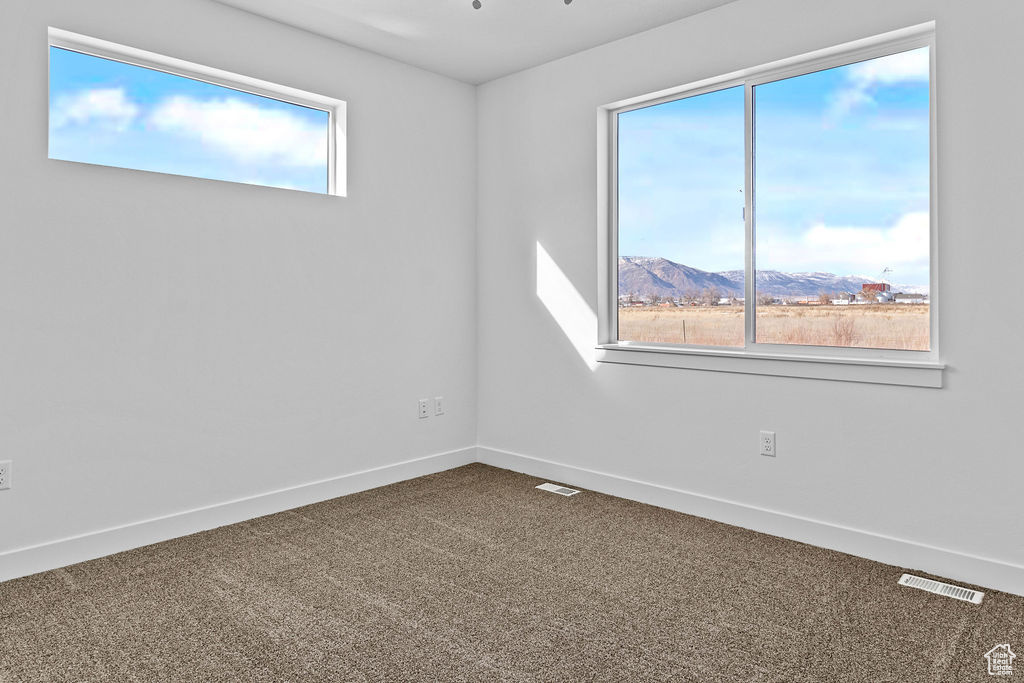 Empty room featuring dark carpet, a wealth of natural light, and a mountain view