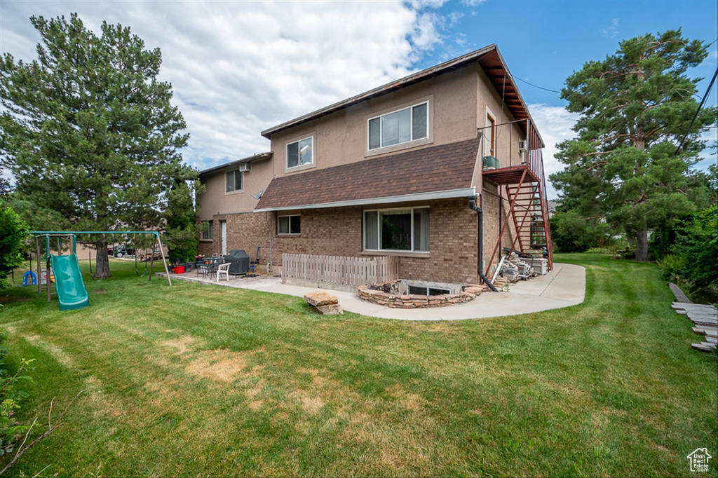 Rear view of property with a playground, a lawn, and a patio