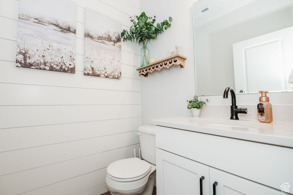 Bathroom featuring wooden walls, toilet, and large vanity