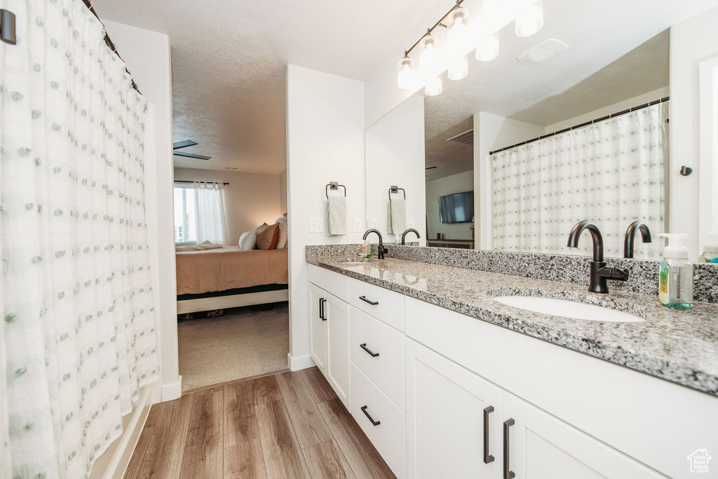 Bathroom with wood-type flooring, dual sinks, large vanity, and ceiling fan