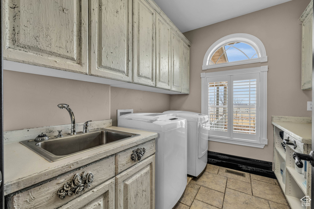 Laundry room with washing machine and clothes dryer, light tile flooring, cabinets, and a healthy amount of sunlight