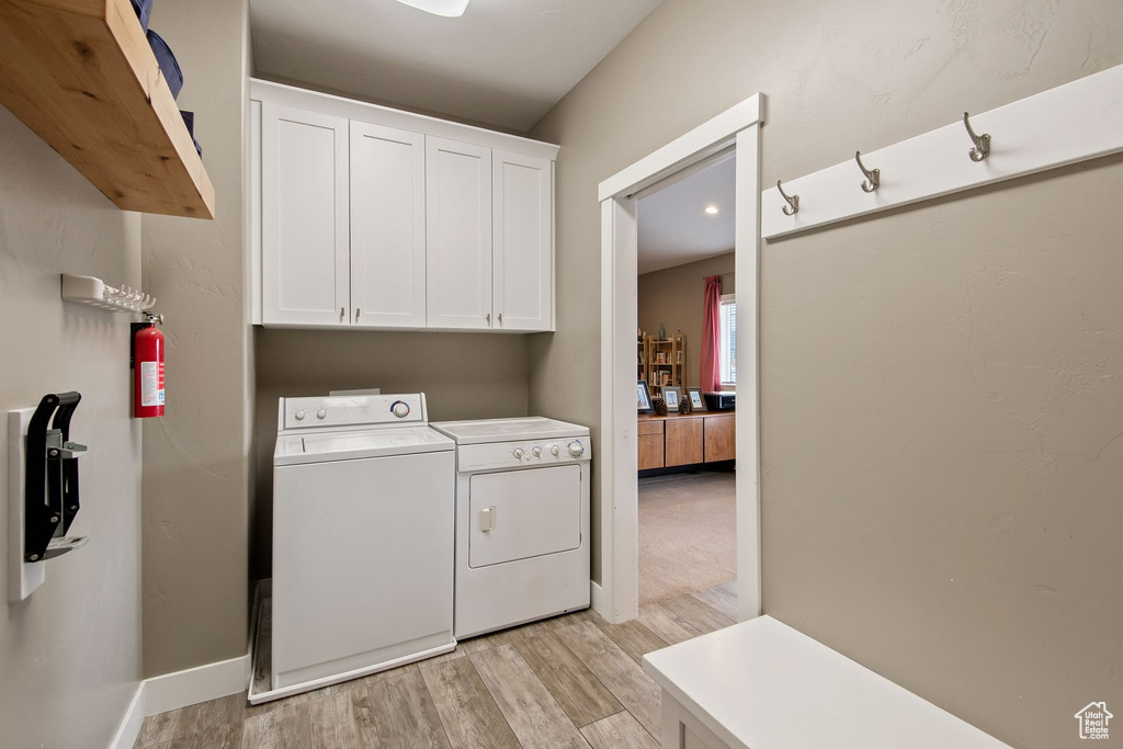 Clothes washing area with light hardwood / wood-style flooring, cabinets, and washing machine and dryer