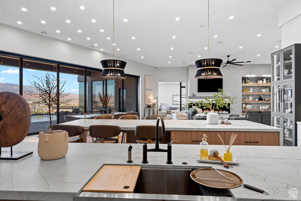 Kitchen with ceiling fan, light stone countertops, a center island, and decorative light fixtures