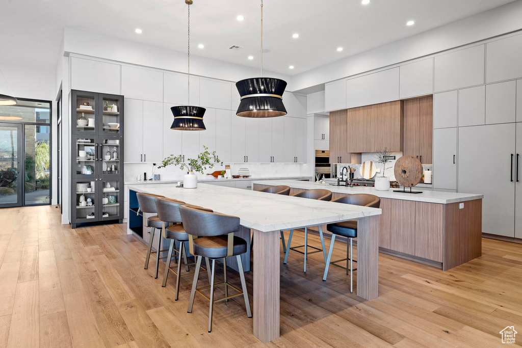 Kitchen featuring a center island with sink, white cabinets, light hardwood / wood-style flooring, and hanging light fixtures