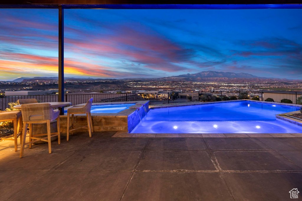 Pool at dusk featuring an in ground hot tub, a patio, and a mountain view