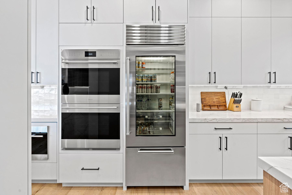 Kitchen with tasteful backsplash, light hardwood / wood-style floors, stainless steel appliances, and light stone counters