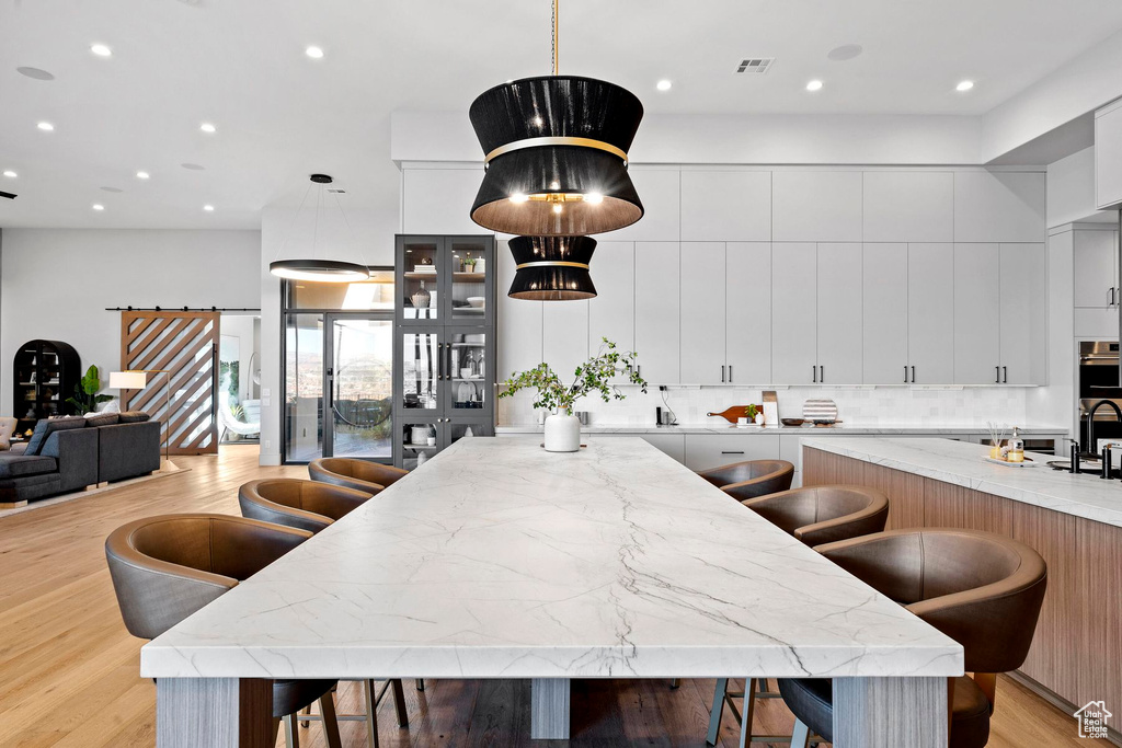 Kitchen featuring light stone counters, pendant lighting, white cabinetry, and a center island