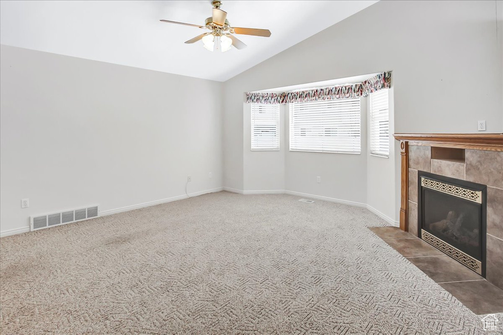 Unfurnished living room with a tile fireplace, dark carpet, lofted ceiling, and ceiling fan