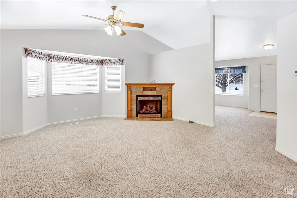 Unfurnished living room with light carpet, a fireplace, vaulted ceiling, and ceiling fan
