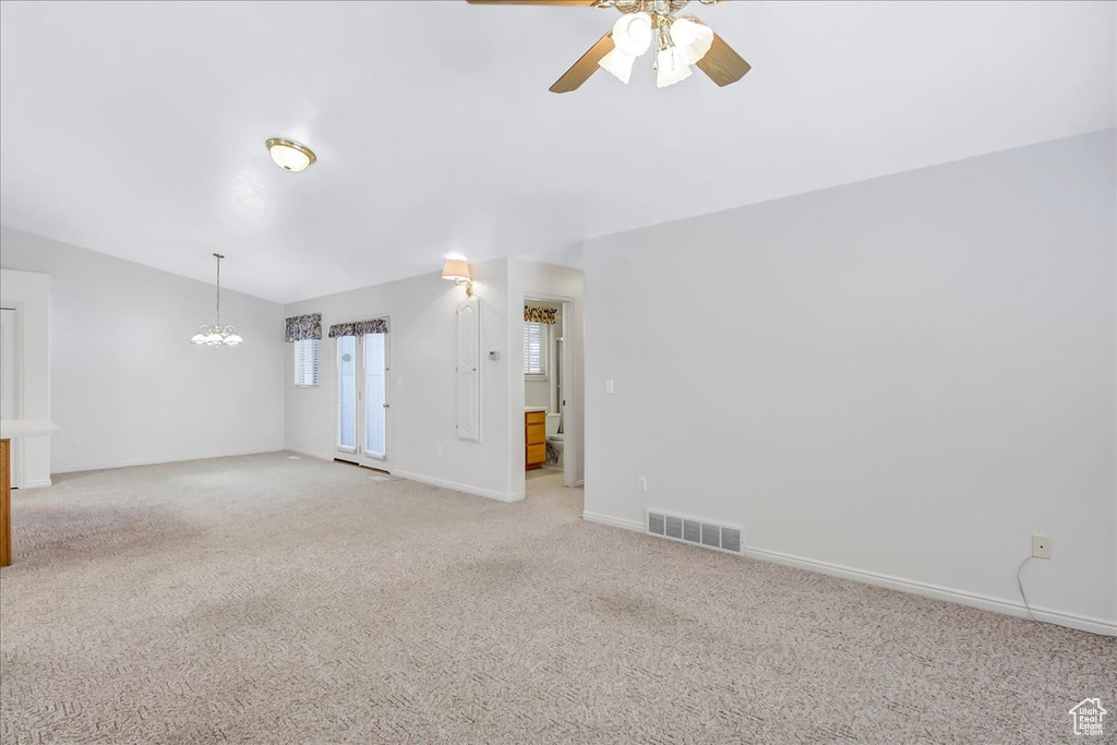 Carpeted spare room with ceiling fan with notable chandelier