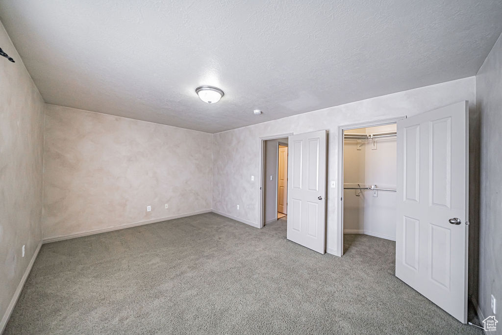 Unfurnished bedroom with a textured ceiling, a closet, a walk in closet, and light carpet