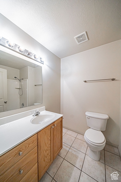 Bathroom with toilet, vanity, tile floors, a textured ceiling, and walk in shower