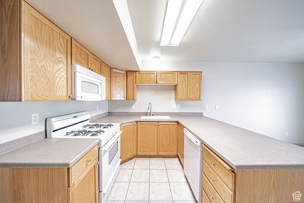 Kitchen featuring light tile flooring, sink, white appliances, and kitchen peninsula