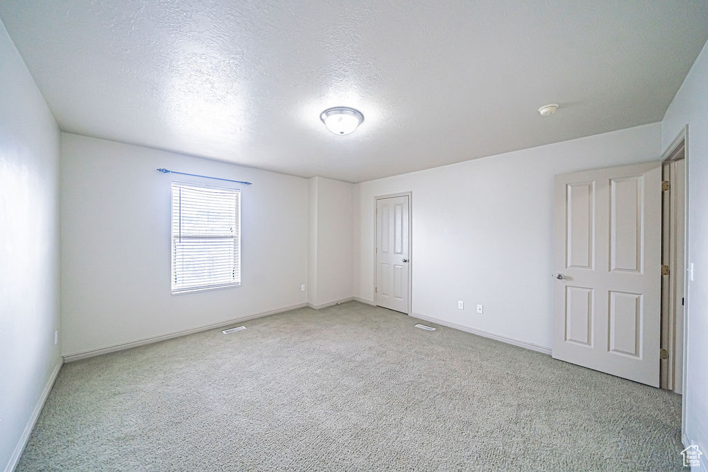 Unfurnished room with a textured ceiling and light colored carpet