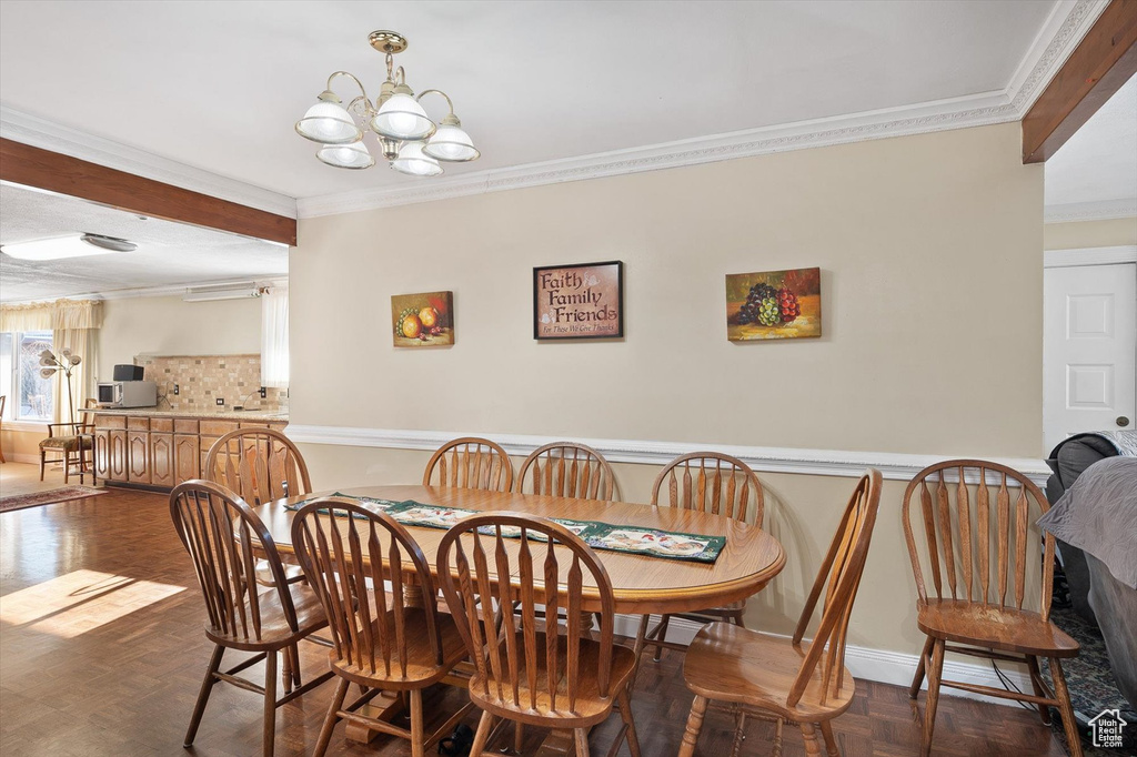 Dining space with dark parquet flooring, a chandelier, and crown molding